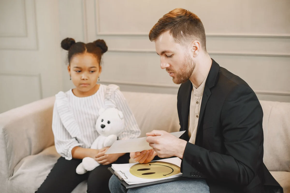 A young girl holding a plush toy during a session with a counselor